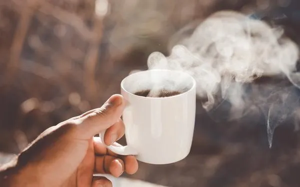 A white ceramic mug filled with steaming coffee in morning light.