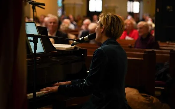 A woman with short blonde hair who is the Director of Contemporary Worship plays the piano and sings in the SMCC sanctuary.