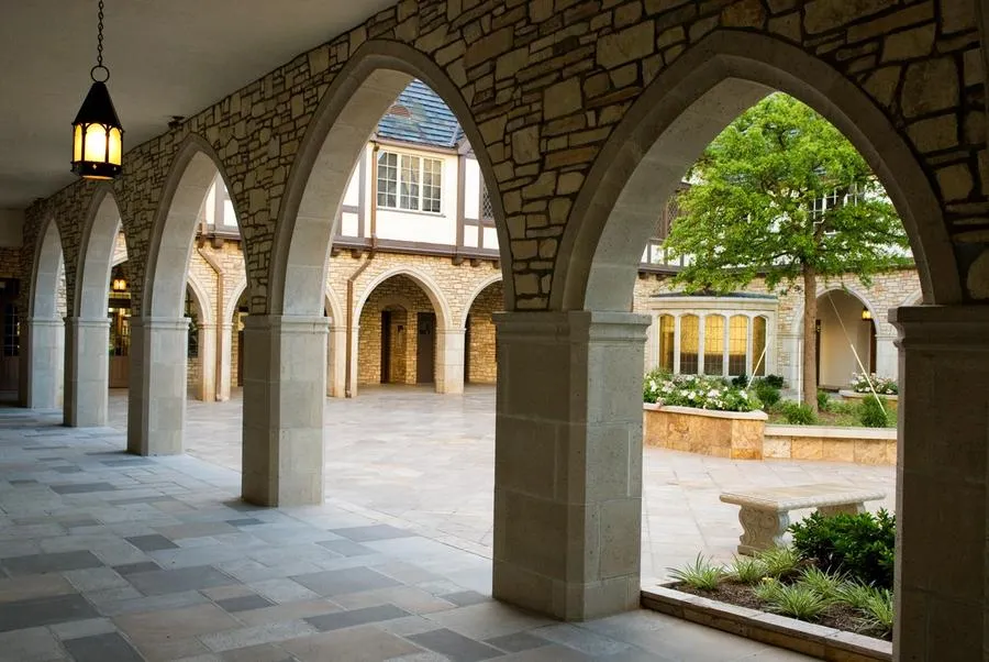 A view into the stone courtyard from inside the stone lined colonnade with pointed arches. A single lantern hangs in the colonnade.