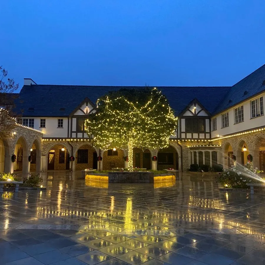 The SMCC courtyard at night. Int he center, a single tree in a stone planter is bedecked with string lights. Christmas wreaths are hung on the columns surrounding the courtyard.