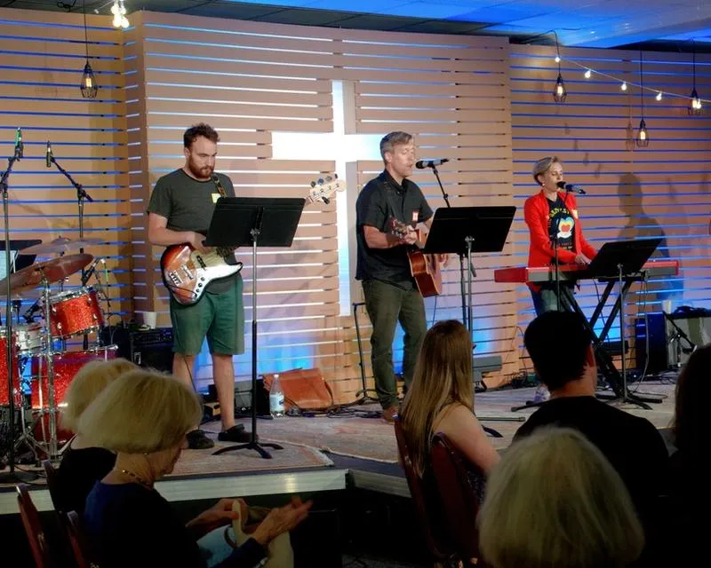 Five members of the Virginia Road Band play electric musical instruments in front of a wood slat wall with a white cross cut out.