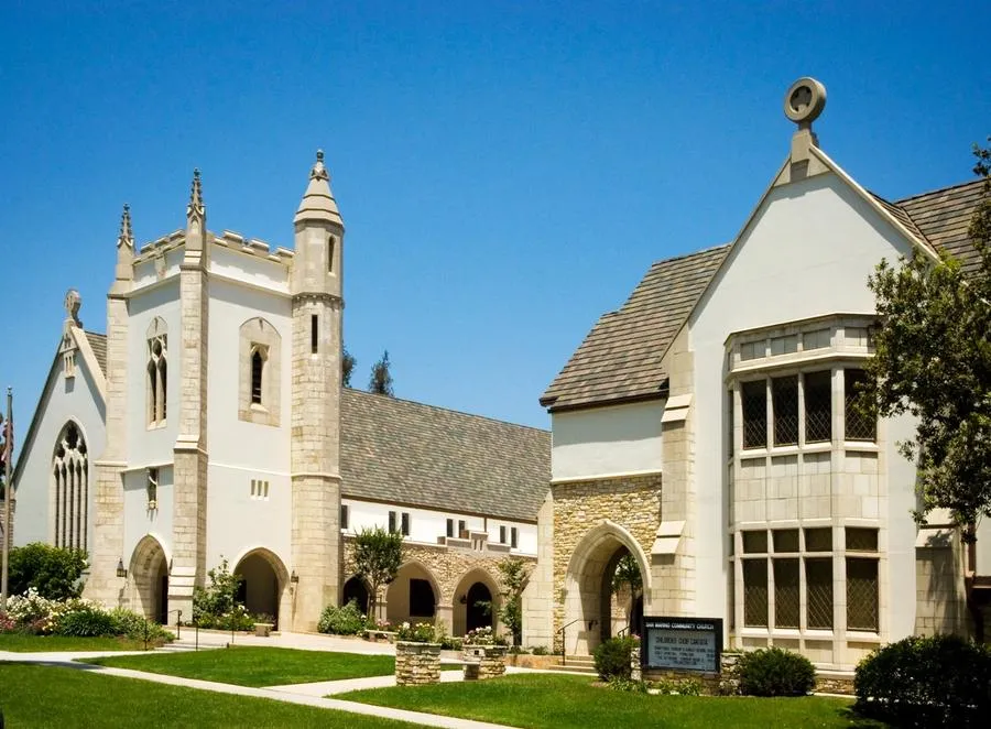 Front exterior of church showing a green lawn and white stone architecture of church.